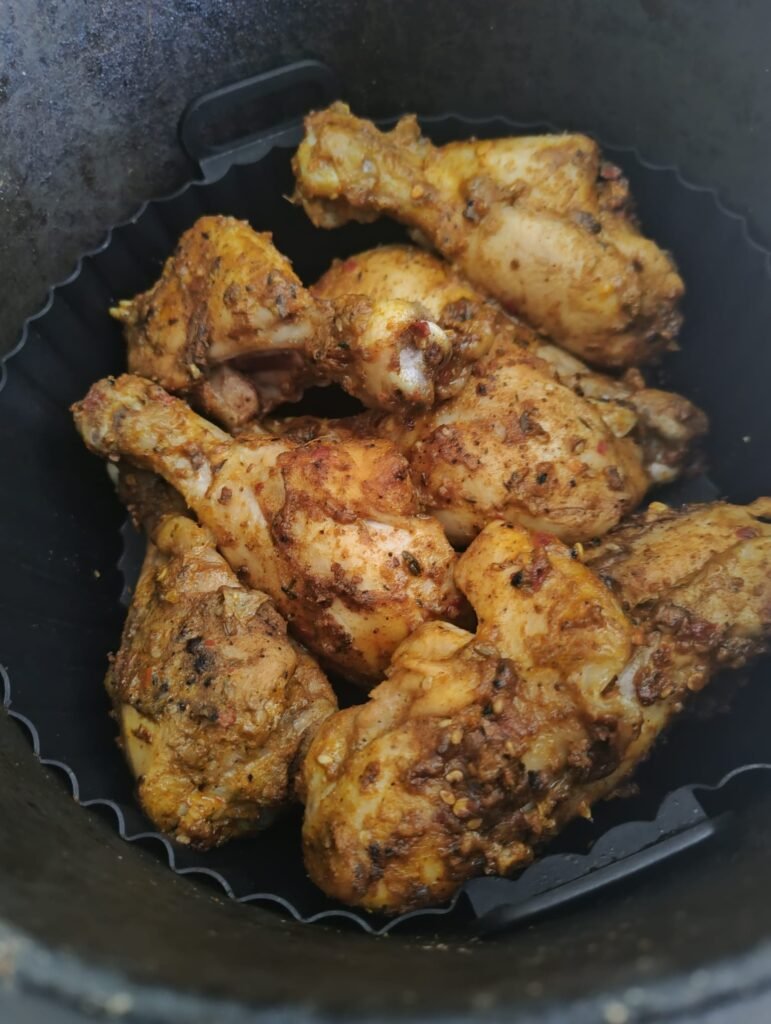 Cooked chicken drumsticks in air fryer basket showing crispy exterior