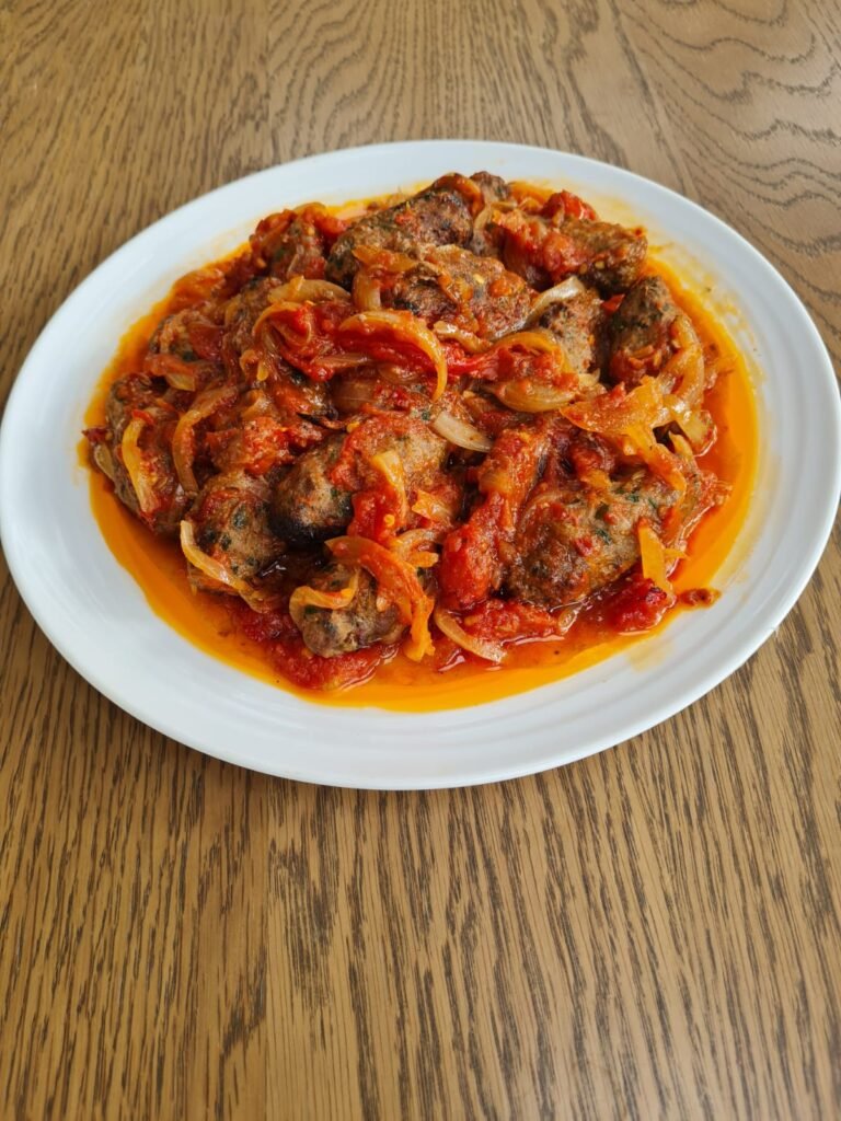lamb kofta in chunky tomato sauce on white plate